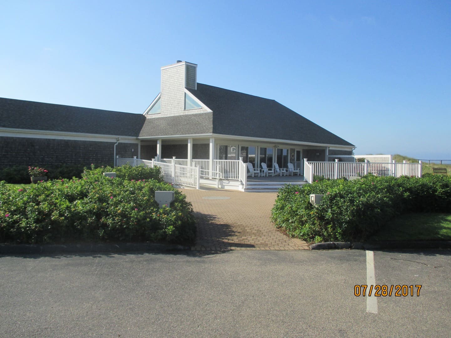 A white building with a large porch and bushes.