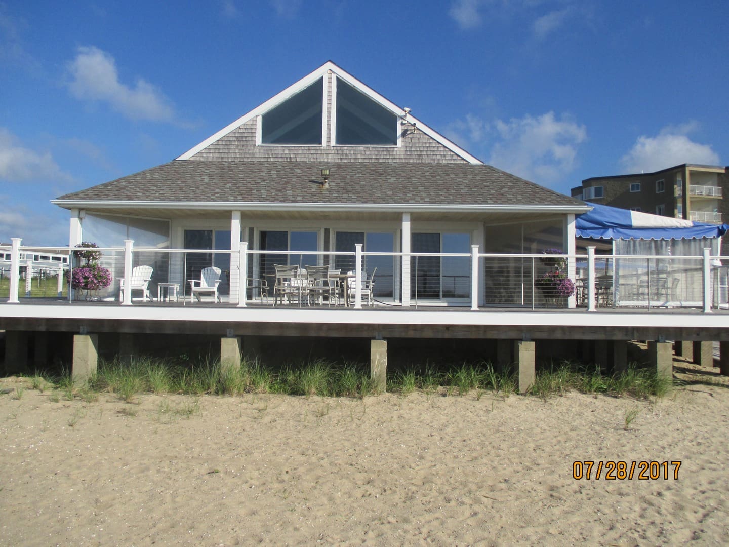 A beach house with a deck and patio on the sand.