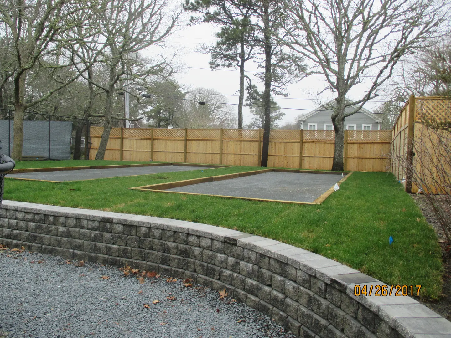 A backyard with grass and trees, concrete walls and a stone wall.