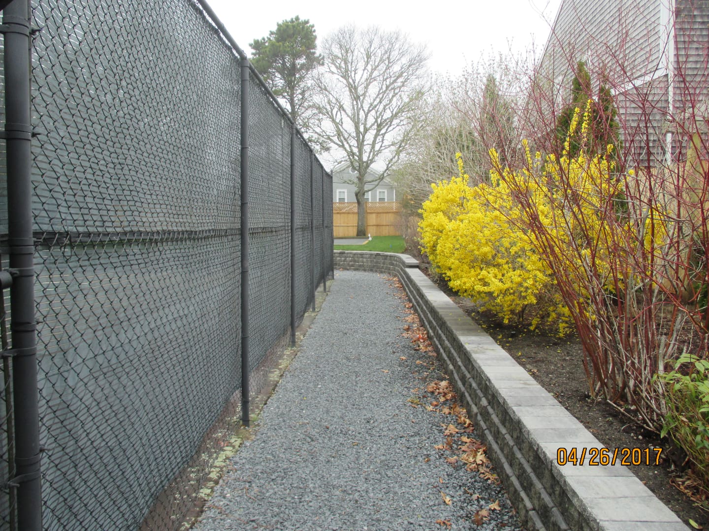 A walkway with a fence and bushes in the background.